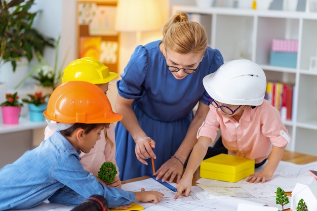 After drawing sketches. Three pupils in bright helmets standing near teacher after drawing sketches