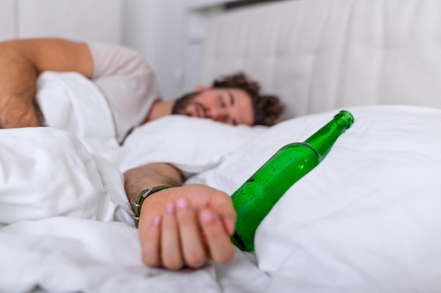 Dopo aver bevuto. uomo adulto barbuto ubriaco sdraiato sul letto e dorme dopo aver bevuto molto alcol, bottiglia vuota sul letto, alcolismo, dipendenza da alcol e concetto di persone