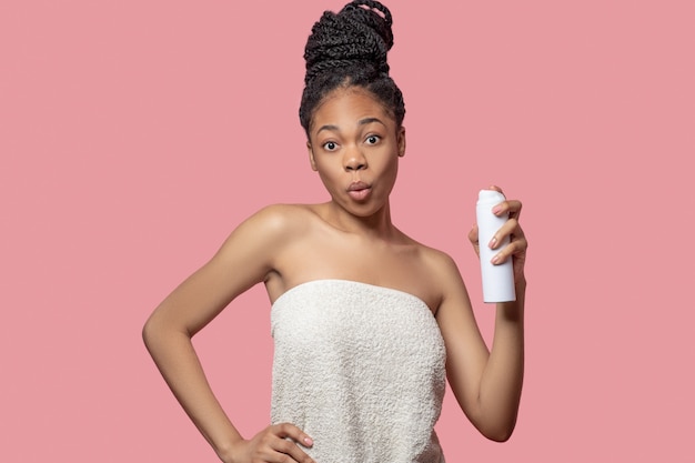 After shower. Dark-skinned young woman spraying deodorant on her body after shower