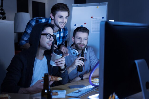 After work. Handsome positive nice men drinking beer and eating pizza while resting after work