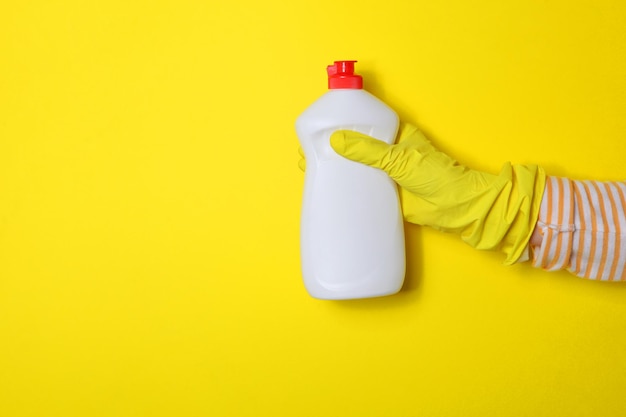 Foto afwasmiddel op een gekleurde achtergrond in vrouwelijke handen in handschoenen