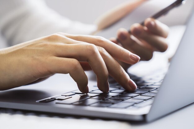 写真 ぼやけたオフィスの背景を背景に、洗練されたノートパソコンのキーボードを入力する女性の手を捉えた画像