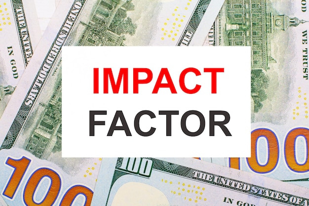 Against the background of American dollars a white card with the IMPACT FACTOR Financial concept