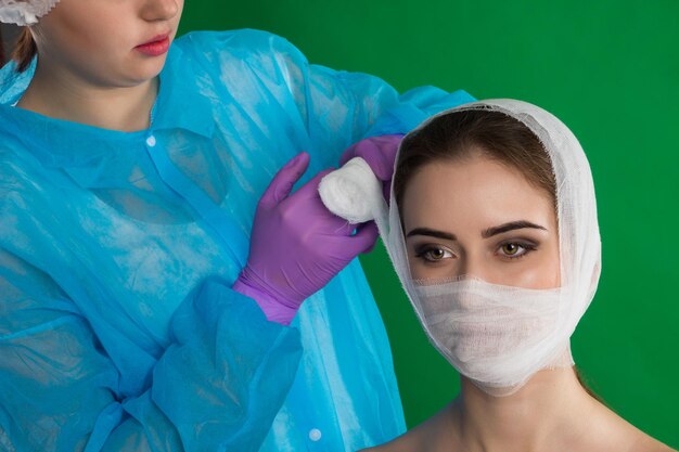 Against the background of chromakey the doctor with violet gloves is binding up the woman with a bandage the woman with beautiful eyes.