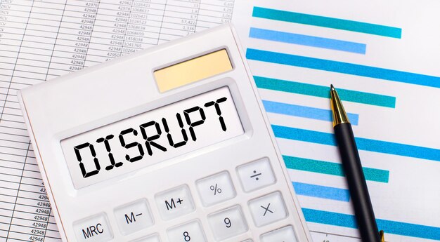 Against the background of reports and blue graphs, a pen and a white calculator with a test on the DISRUPT screen. Business concept