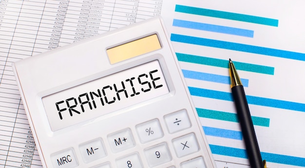 Against the background of reports and blue graphs, a pen and a white calculator with a test on the FRANCHISE screen. Business concept