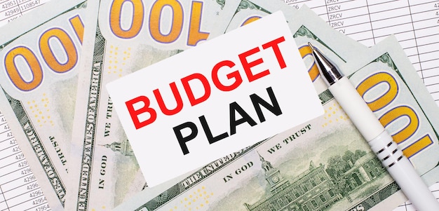 against the background of reports and dollars - a white pen and a card with the text budget plan. business concept