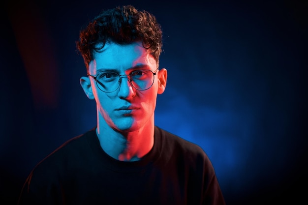 Against black background Neon lighting Young european man is in the dark studio