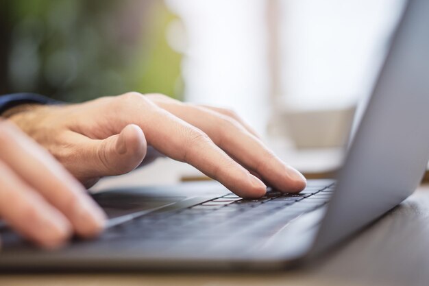 Against a blurry office backdrop a closeup view reveals a man's hands as they type on a sleek laptop keyboard