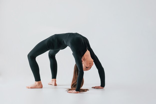 Against white background Young woman in sportive clothes doing gymnastics indoors