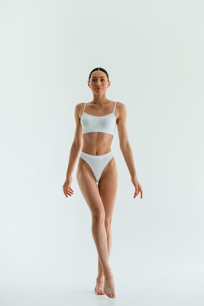 Against white background Young woman with slim body type is in fitness clothes in the studio
