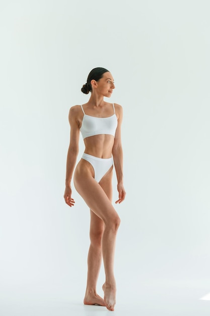 Against white background Young woman with slim body type is in fitness clothes in the studio