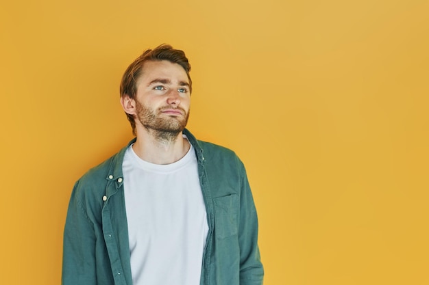 Against yellow background Young man in casual clothes standing indoors in the studio