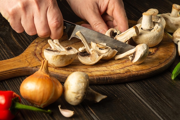 Agaricus-paddenstoelen op snijplank snijden door handen van chef-kok met mes om een heerlijk gerecht te bereiden