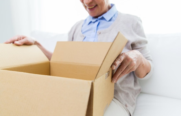 age, delivery, mail, shipping and people concept - close up of happy smiling senior woman looking into open parcel box at home