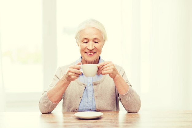 age, drink and people concept - happy smiling senior woman with cup of coffee at home