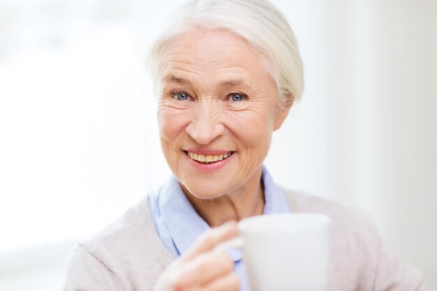 age, drink and people concept - happy smiling senior woman with cup of tea or coffee at home