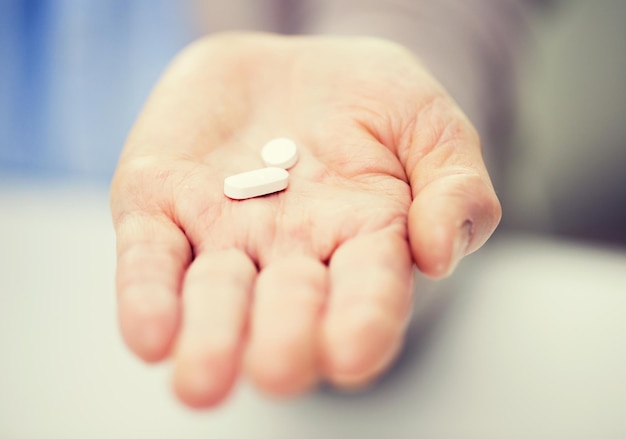 age, medicine, health care and people concept - close up of senior woman cupped hand with pills at home or hospital