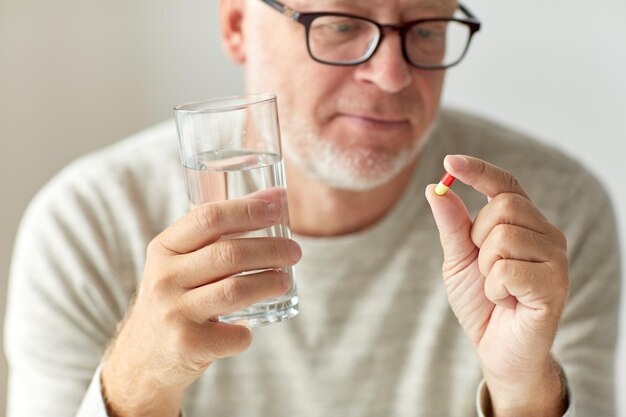 age, medicine, healthcare and people concept - close up of senior man hands with pills and water