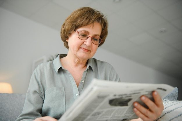 Age and people concept happy senior woman reading newspaper at home