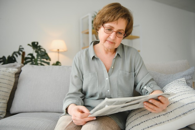 Age and people concept happy senior woman reading newspaper at home