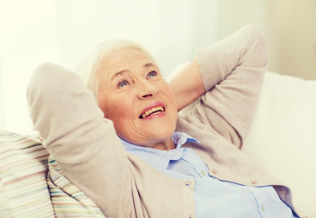 age, relax and people concept - happy smiling senior woman resting on sofa and dreaming at home