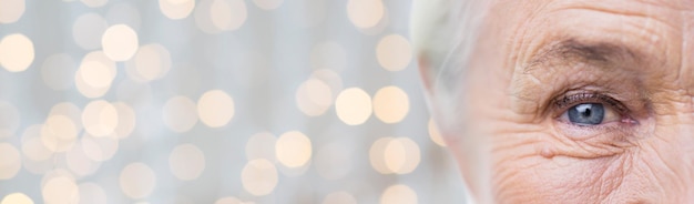 Photo age, vision and old people concept - close up of senior woman face and eye over holidays lights background