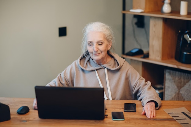 Photo aged elderly woman with laptop and mobile phone working on computer at table