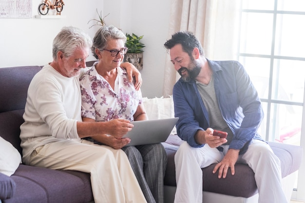 Aged family scene at home with mother father adult mature senior and son middle age with beard enjoy together the technology with laptop computer and mobile phone