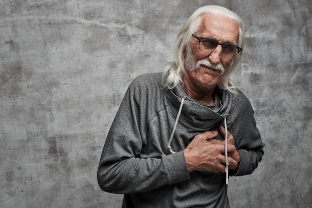 백발의 백인 남성 연금 수급자는 심장마비로 인한 고통으로 가슴을 잡고 있습니다. 콧수염 안경 쓴 할아버지 뇌졸중