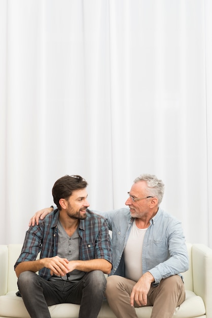 Photo aged man hugging young guy on sofa