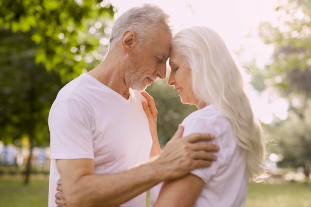 Aged man and woman in the park closing eyes and their foreheads touching