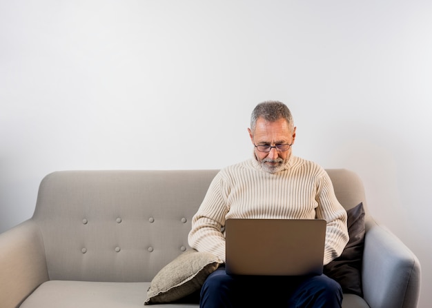 Uomo invecchiato che lavora al suo computer portatile con copia-spazio