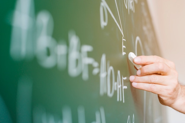 Photo aged math teacher writing formula on chalkboard