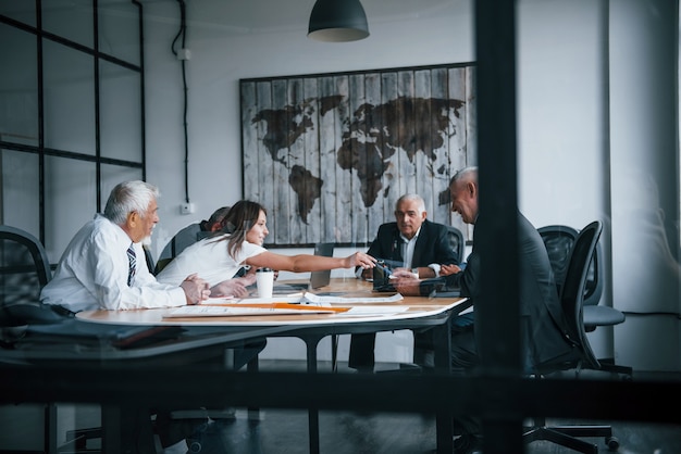 Aged team of elderly businessman architects have a meeting in the office and works with young woman.