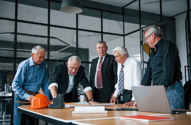 Aged team of elderly businessman architects works with plan in the office.