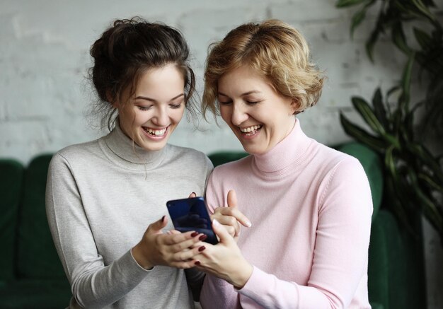 Photo aged woman and her adult daughter using smartphone at home