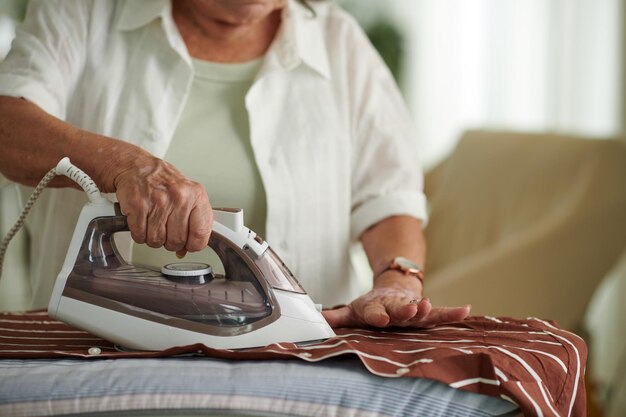 Aged woman ironing shirt before work