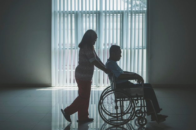 Пожилая женщина толкает мужа на инвалидной коляске