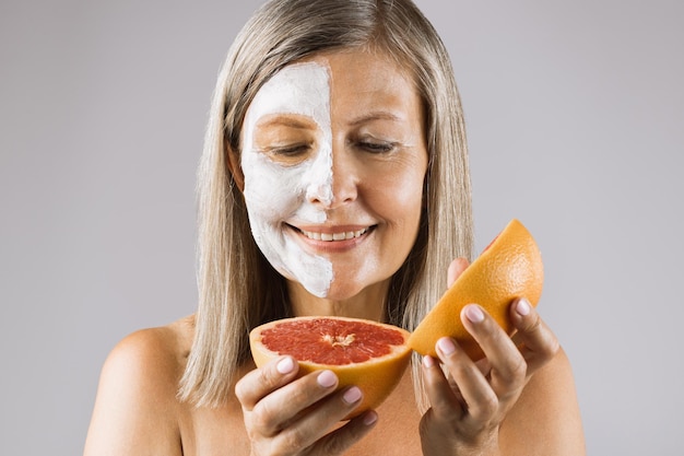Aged woman with mask on half face holding grapefruit