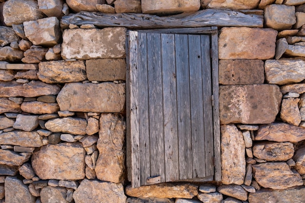 Aged wooden closed shutter old stone wall rural building background at Gavdos island Crete Greece