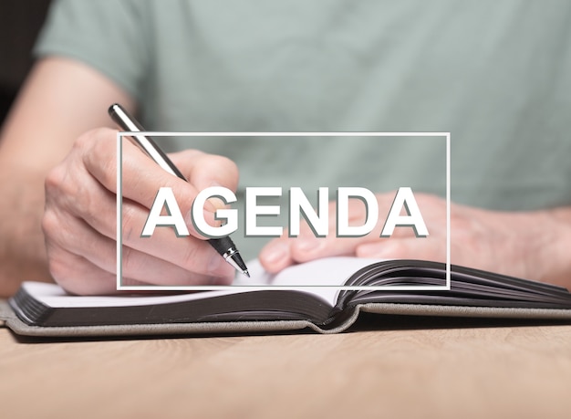 Agenda word with photo of male hands writing in planner or organizer.