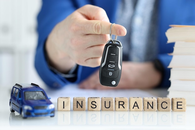 単語保険のクローズアップ自動車保険が必須の木製の立方体の近くに車のキーを保持しているエージェント