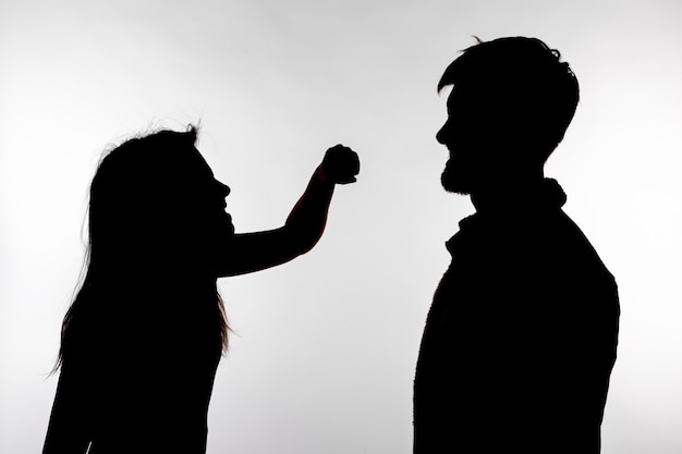 Концепция агрессии и жестокого обращения - мужчина и женщина, выражающие насилие в семье в силуэте студии, изолированном на белом фоне.