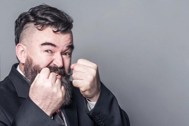 Aggressive adult bearded man in a suit showing fists on a red background