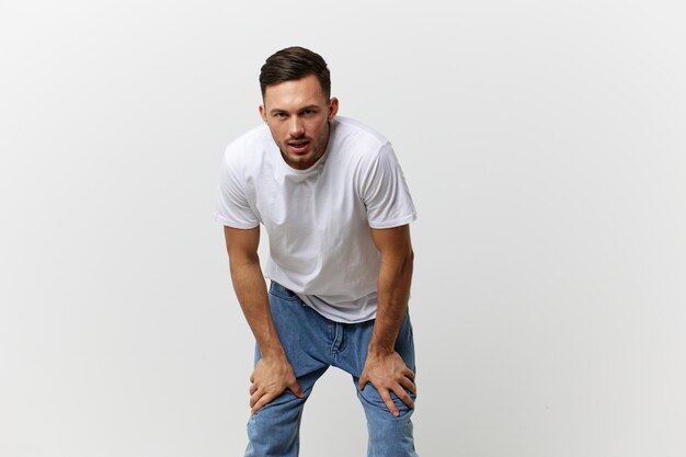 Aggressive angry evil tanned handsome man in basic tshirt leans\
on knees posing isolated on over white studio background copy space\
banner mockup people emotions lifestyle concept