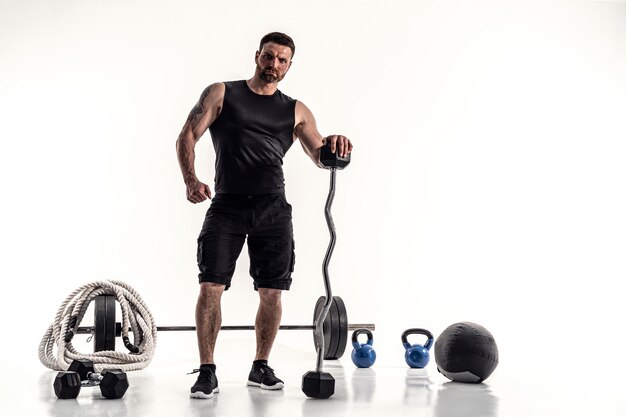 Aggressive bearded strong muscular Man in sportswear with barbell and sport equipment on white isolate.