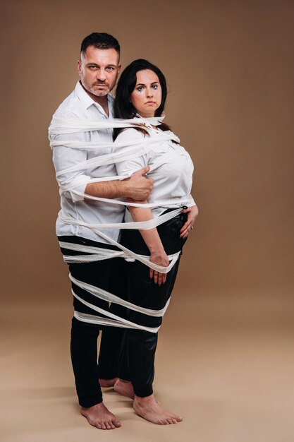 An aggressive man embraces a battered woman and is wrapped in bandages together. domestic violence.