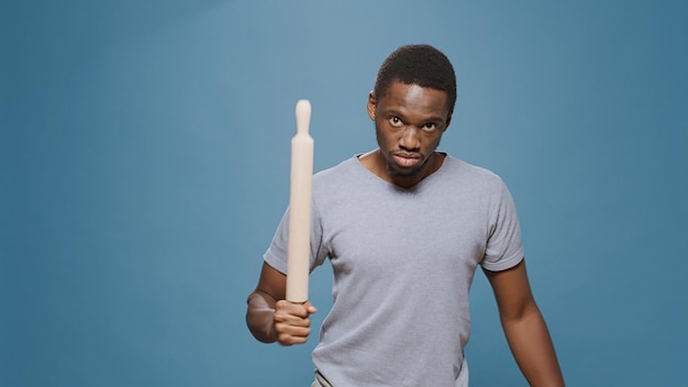 Aggressive upset rebel raising paddle at camera to fight, instigating violence and criminal activity in studio. Furious male bully with clenched fists doing fighting demonstration to protest.