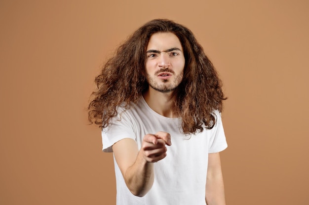 Aggressive young guy pointing finger at camera over beige background